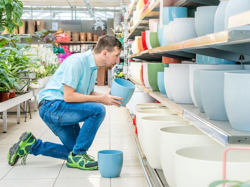 Eine Arbeitskraft sortiert Blumentöpfe in ein Regal ein